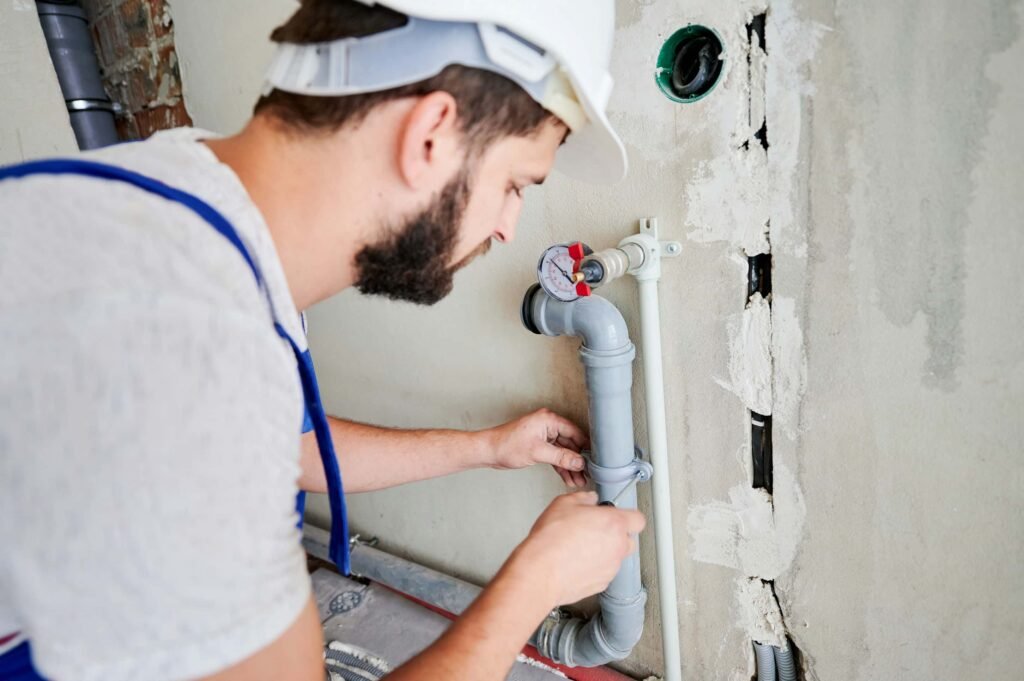 male plumber tightening a clamp on a pipe with a screwdriver