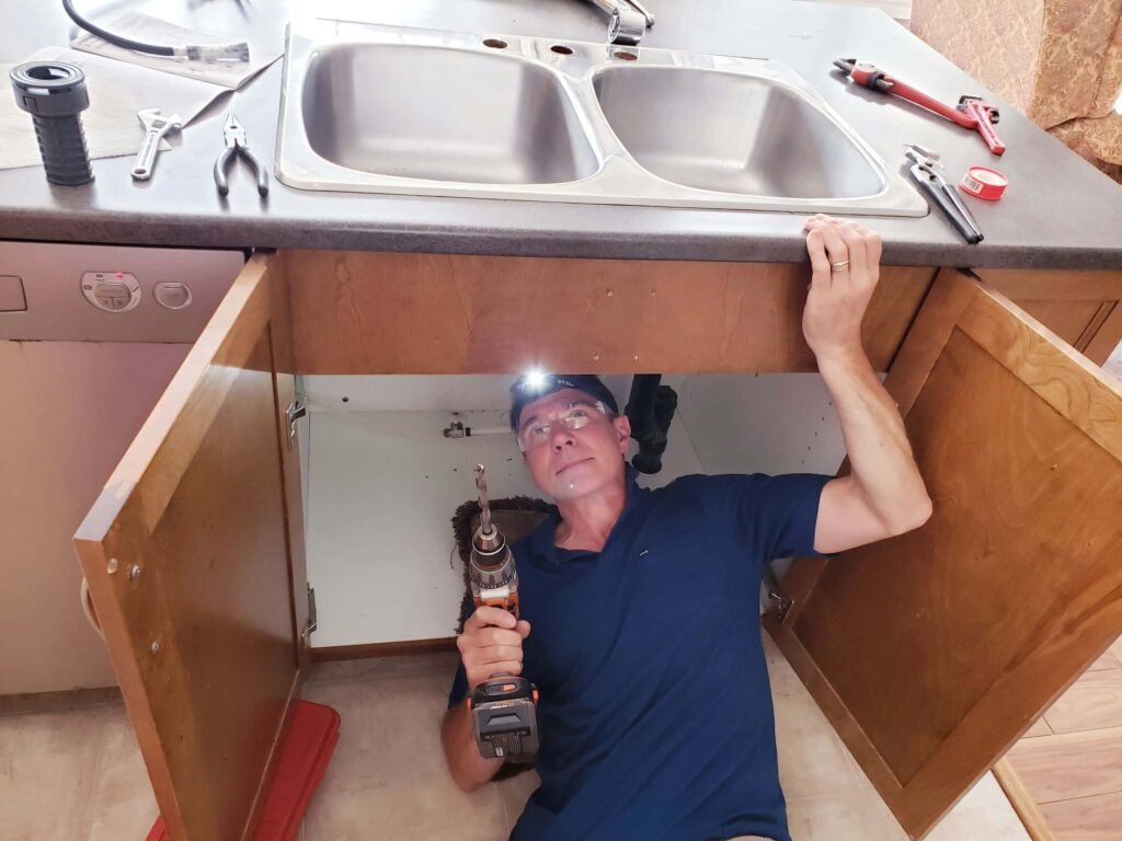 man repairing a sink leak under the sink using a headlamp